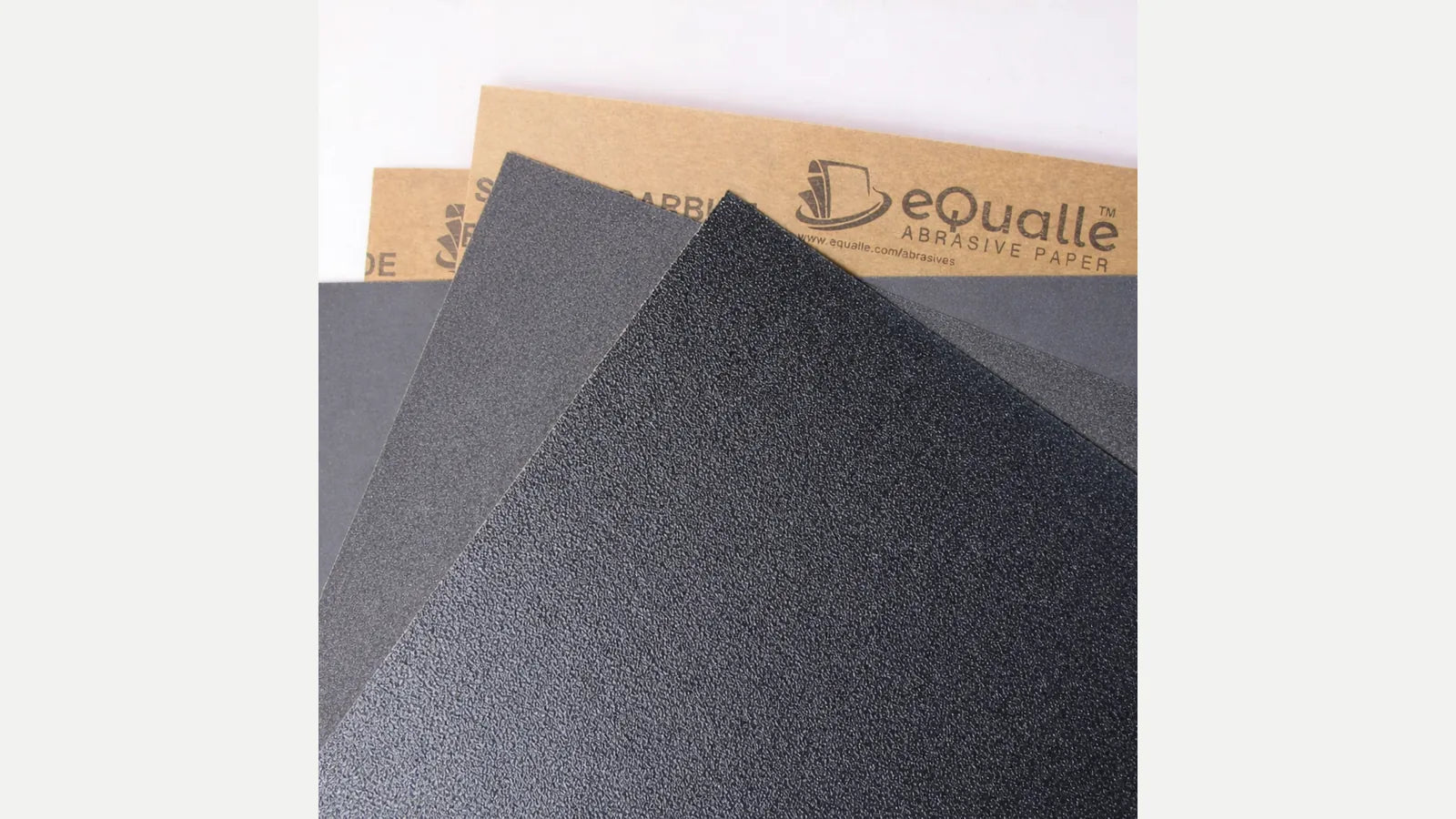 Close-up of overlapping dark abrasive sheet faces and tan eQualle-printed paper backing.
