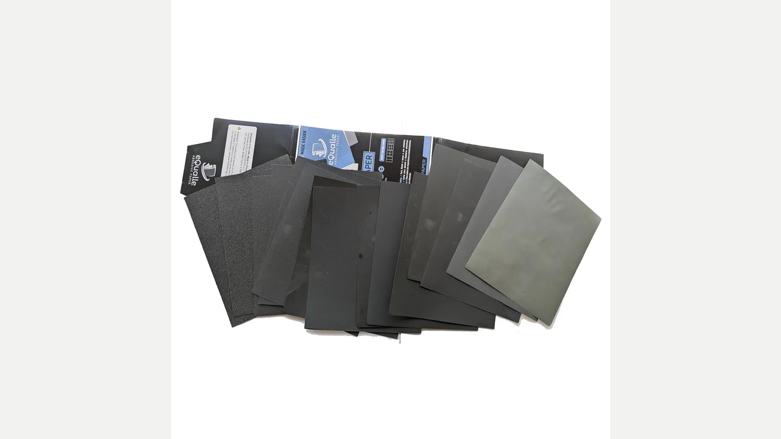Fan of dark abrasive sheets with open blue-and-black eQualle packaging on white.