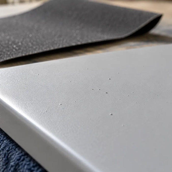 Small surface irregularities on a gray-coated sample with abrasive paper behind it.