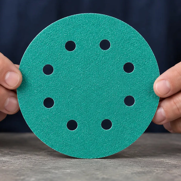Hands holding a green eight-hole abrasive disc for inspection.